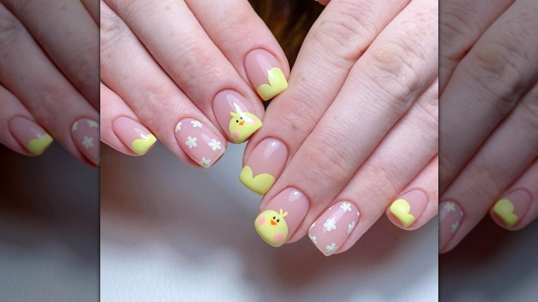 Two angled hands showing a negative-space nail design featuring white flowers and cutesy chicks