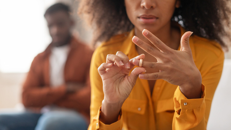 Woman takes off her wedding ring as her husband looks on in the background