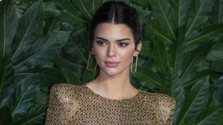 Kendall Jenner wearing gold with greenery behind her
