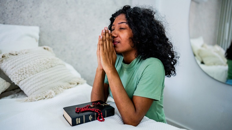 A person praying at the side of their bed over a bible and rosaries