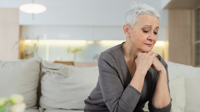 An older woman sitting on a couch and looking sad