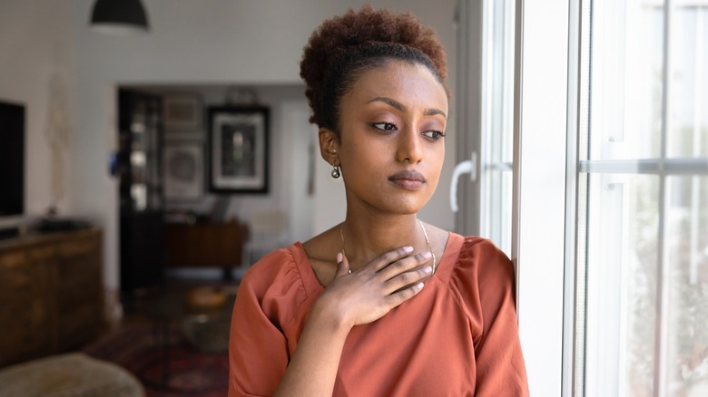 A woman looking out a window with her hand over her chest