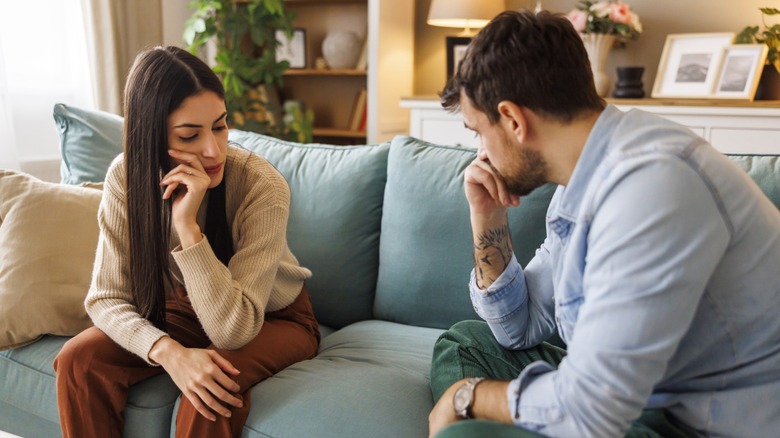 A couple sitting on either side of a couch looking upset