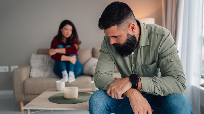 A couple sitting apart (with the man in the foreground) and looking upset