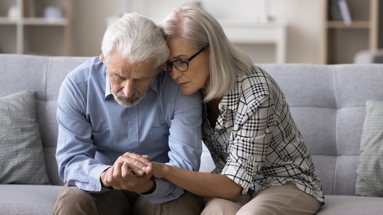 An older couple comforting one another while sitting on a couch