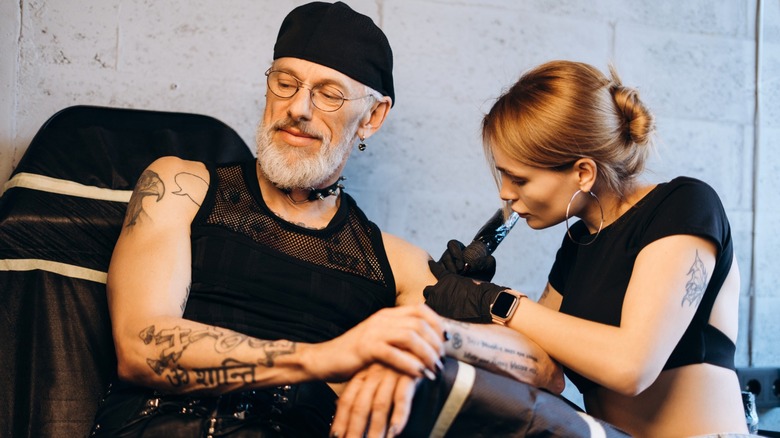 A younger woman giving an older man a tattoo
