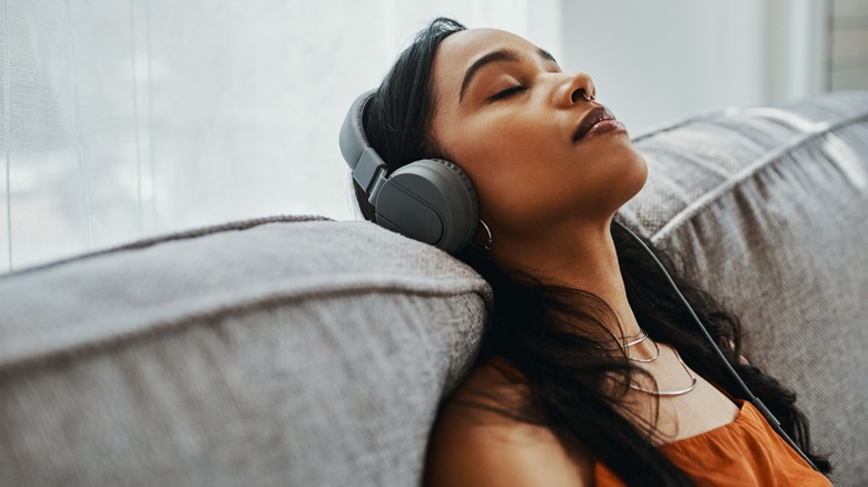 A woman resting her head on a sofa while listening to music through overear headphones