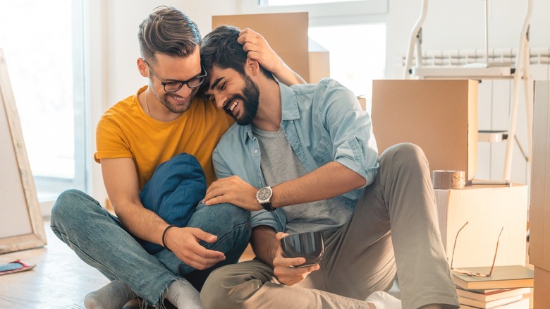 Two men smiling while sitting on the floor surrounded by boxes