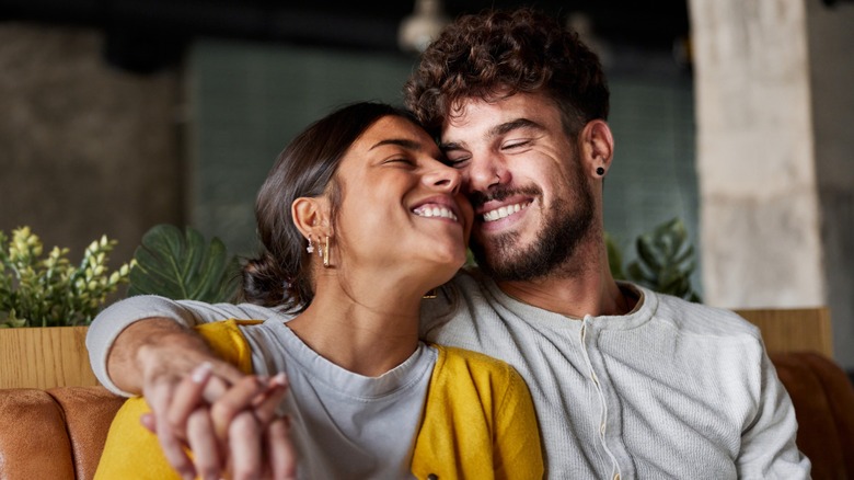 A couple smiling while sitting in a booth, the man has his arm around the woman