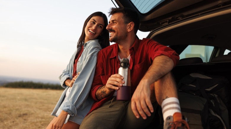 A couple smiling at one another while sitting in the trunk of a car