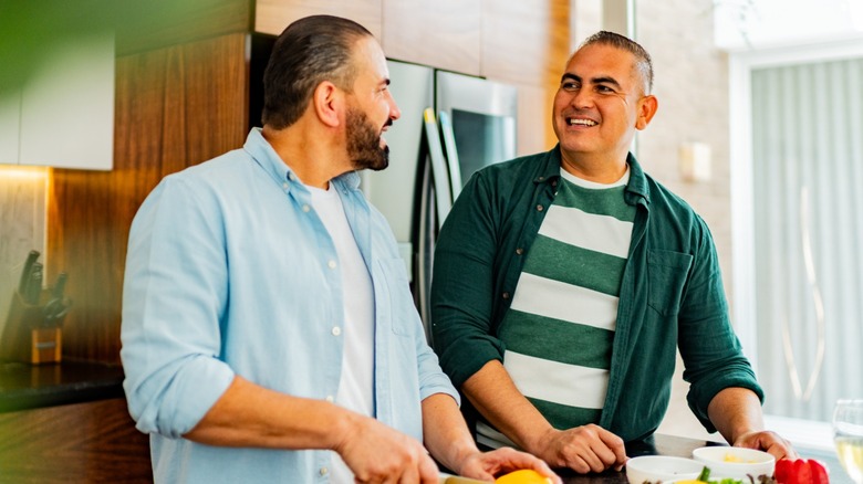 Two men smiling and cooking together in a kitchen
