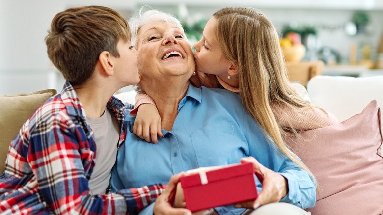 An older woman being kissed on both cheeks by her grandchildren while holding a birthday gift