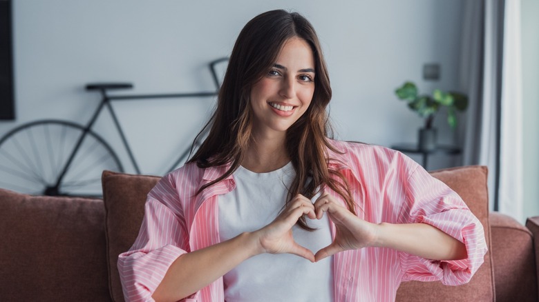 A woman smiling and using her hands to make a heart shape over her chest