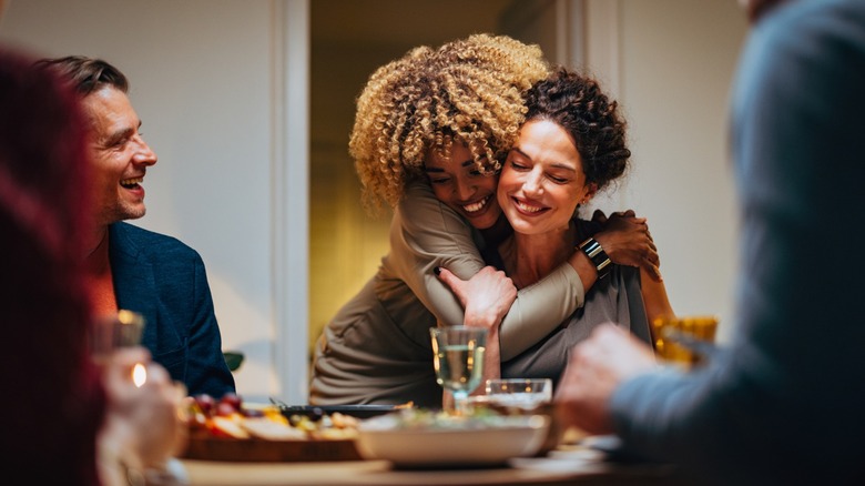 Two friends sharing a hug while sitting around a table