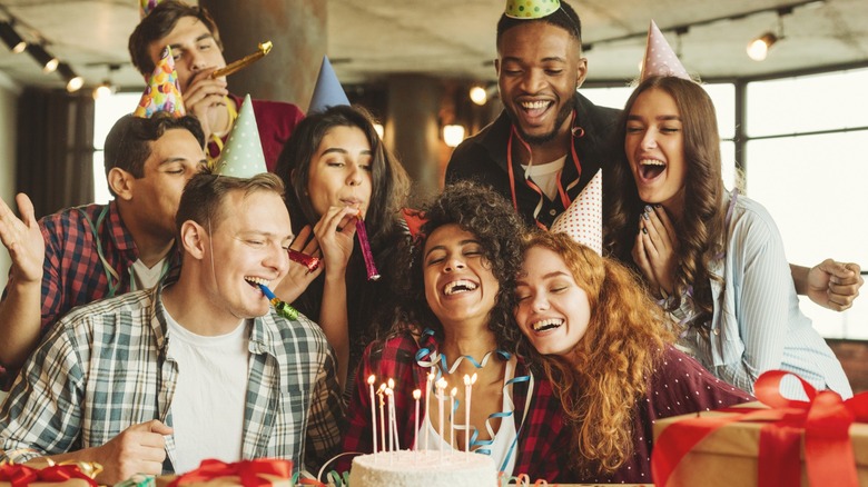 A group of friends smiling while gathered around a birthday cake with lit candles