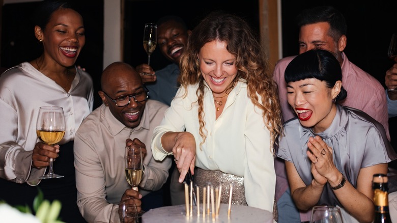 A group of friends gathered around a birthday cake as the candles are lit
