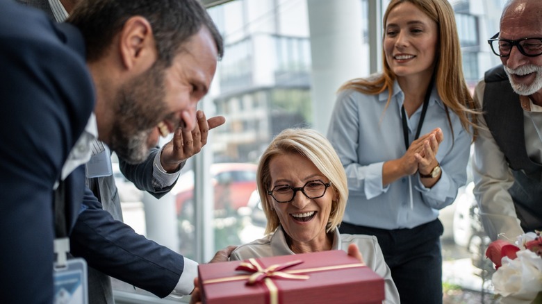 A woman being handed a birthday gift by her co-workers in an office