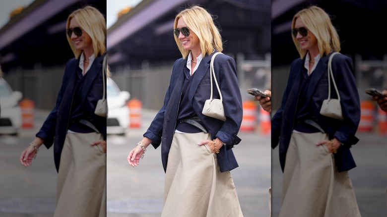A woman carrying a cream shoulder bag with a blue jacket and cream skirt