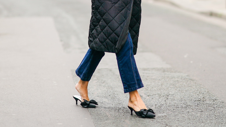 A woman wearing a black jacket, black mules and a blue hat