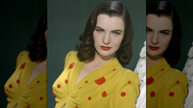Vintage, colored photograph of Ella Raines gazing into the camera while wearing a yellow, polka-dotted blouse