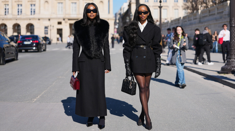 Two stylish women in black ensembles and sunglasses