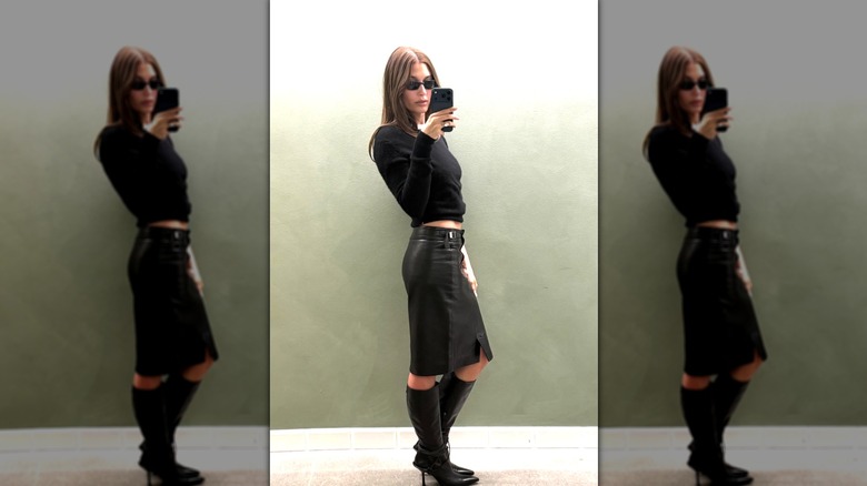 Hailey Bieber wearing a black leather skirt and black boots with a black knit sweater