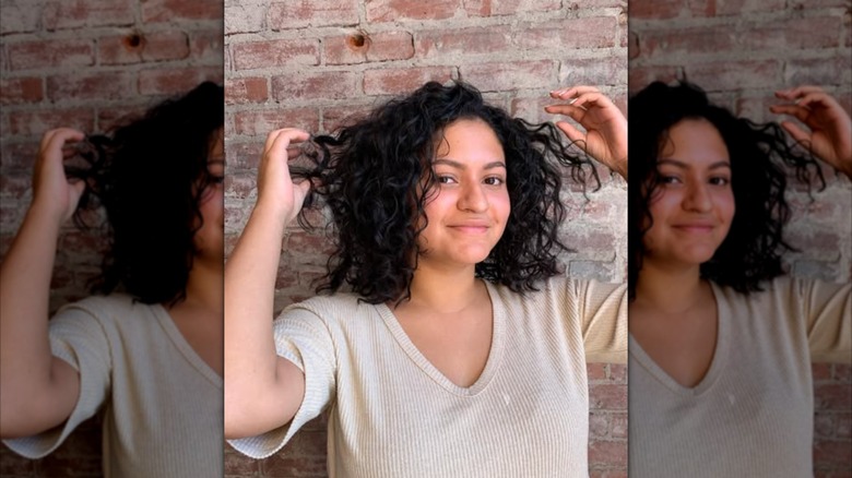 A woman in front of a brick wall with curly dark hair that is shoulder length