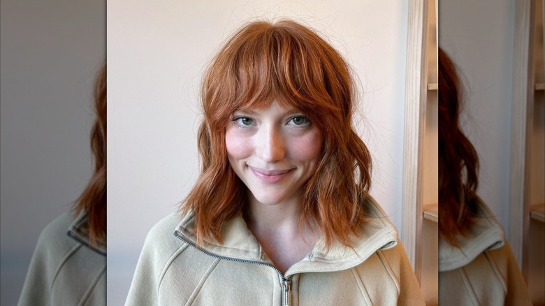 A woman with textured, shoulder-length red hair and bangs