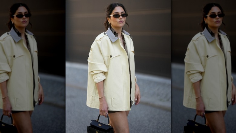 Woman in butter yellow jacket and black bag with oval sunglasses