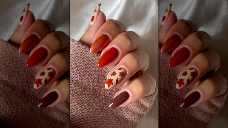 A single folded hand showing a fall-inspired nail designs with solid colors and leaf drawings