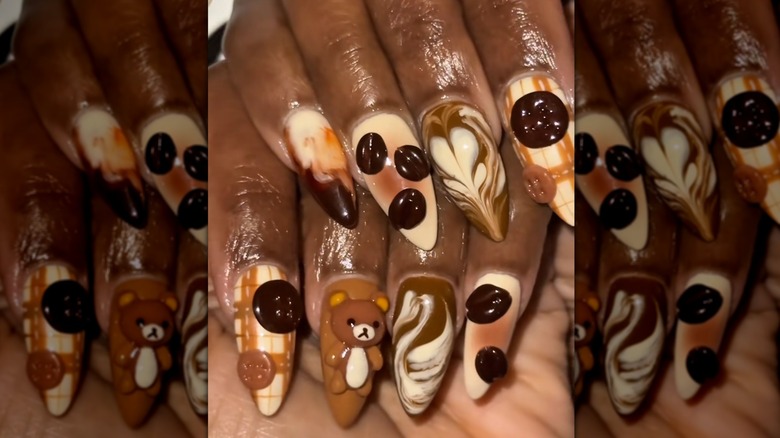 Two folded hands showing a coffee-inspired nail set featuring 3D charms