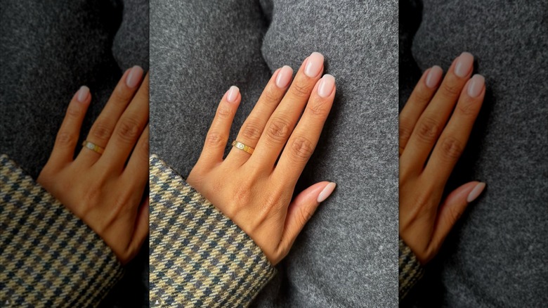 A hand with pink nails with square-rounded tips and a gold ring