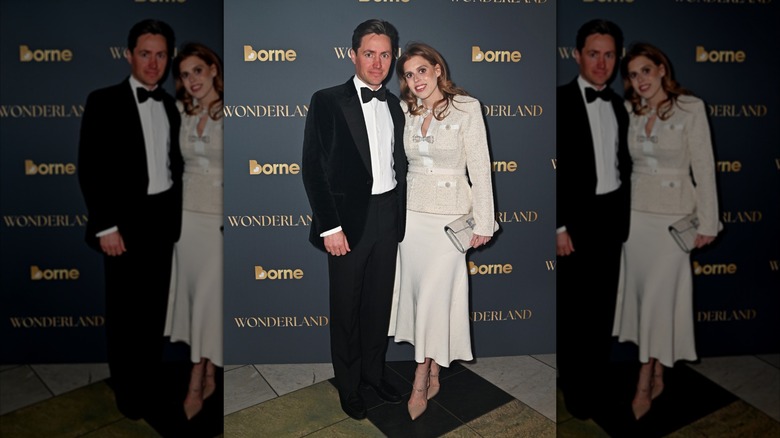 Beatrice wears beige pumps and jacket with bows next to husband