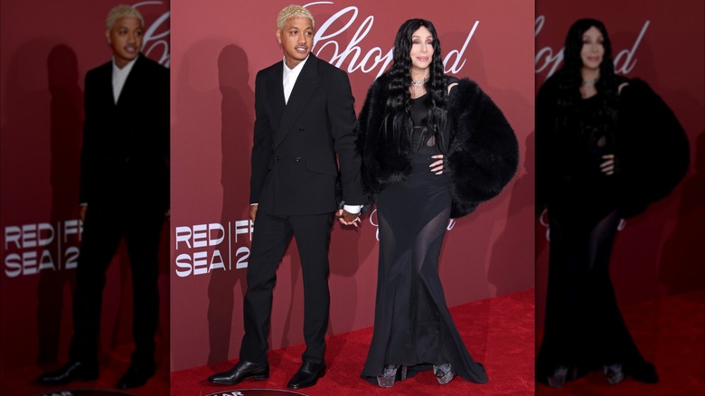 Cher stands with Alexander Edwards wearing a black sheer dress and black fur coat