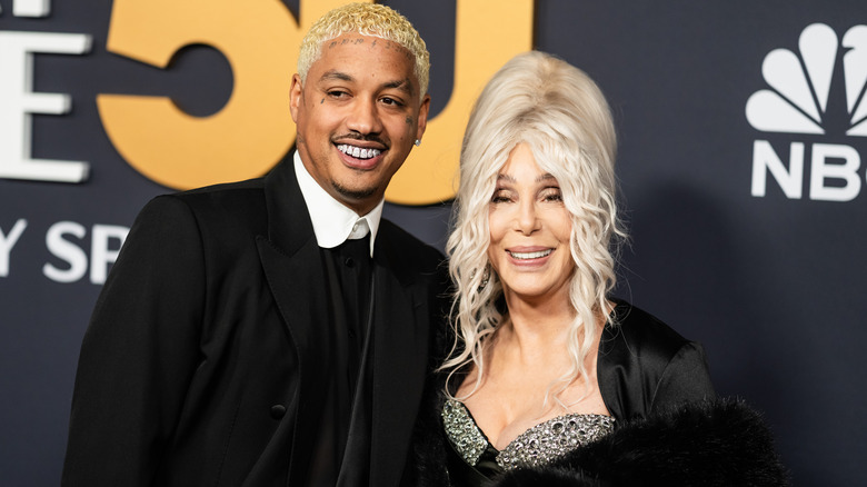 Cher smiles with white hair, next to Alexander Edwards with blonde hair