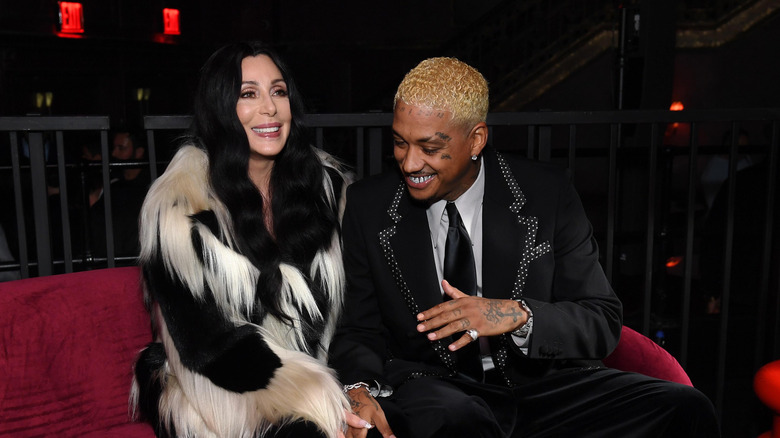 Cher smiles wearing a black and white fur coat next to Alexander Edwards in an embellished blazer