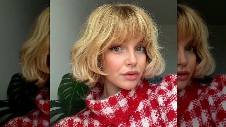 A blonde woman with a French bob and blunt cut bangs looking at the camera