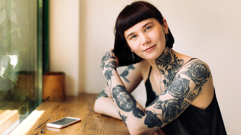 A woman with short brown hair, bangs, and tattoos