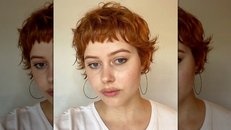 A woman with red hair cut into a pixie style looking at the camera