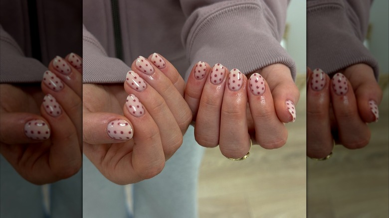 Two hands showing short nails with muave-colored polka dots