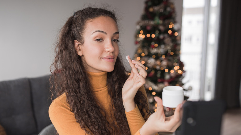 Woman applying skincare by Christmas tree