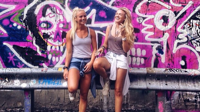 Erika Kirk posing in short shorts with a friend in front of a graffiti wall