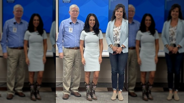 Lauren Boebert in a mint green dress and cowboy boots, standing next to others in front of a screen