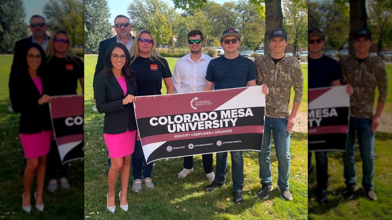 Lauren Boebert in a pink dress and black blazer with others holding a sign