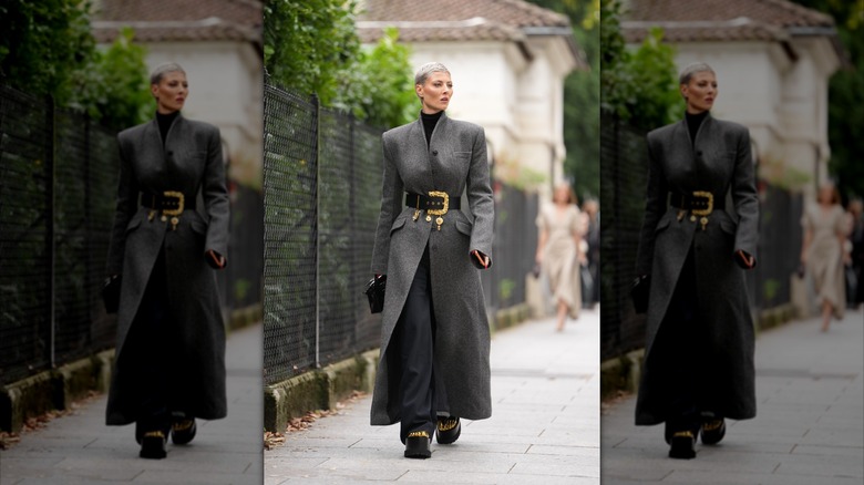 A woman walking down the street in an oversized coat cinched with a statement belt