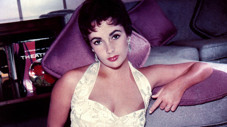 Elizabeth Taylor wearing a white halter top and leaning on a couch cushion