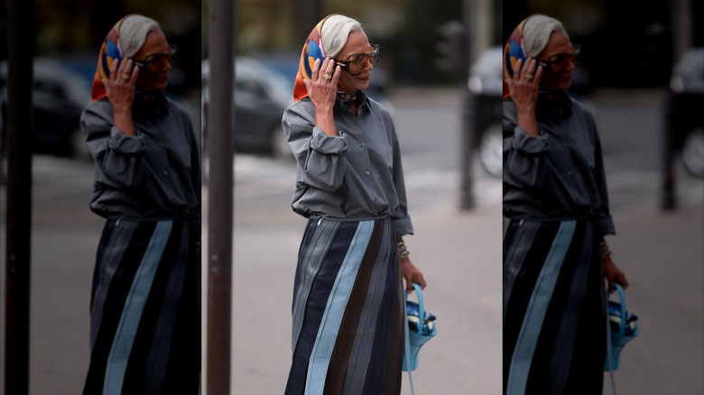 A woman wearing a silk headscarf and oversized sunglasses standing on the street