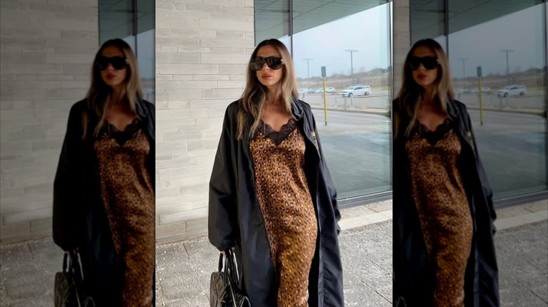 A woman wearing a leopard-print silk slip dress underneath a black trench