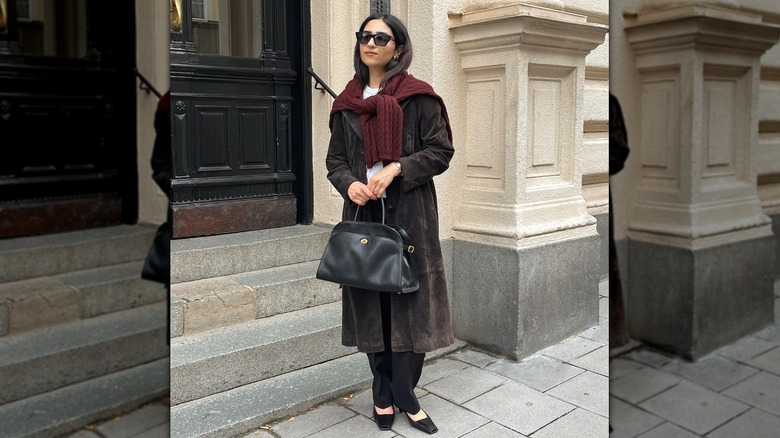 A woman in a long coat with a sweater over her shoulders