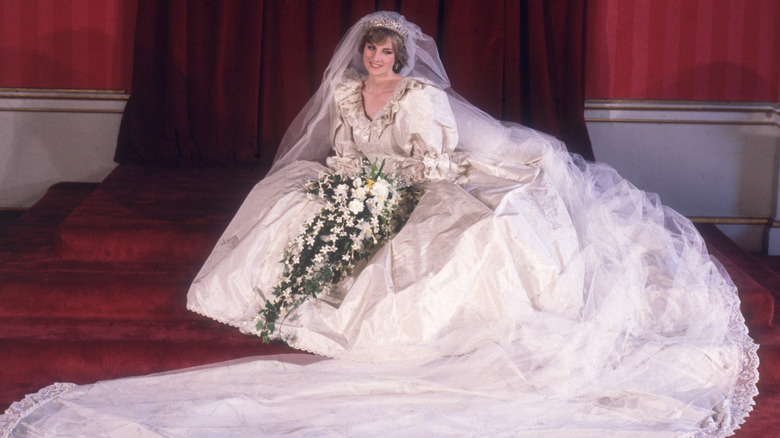 Princess Diana sits in her voluminous wedding dress holding flowers